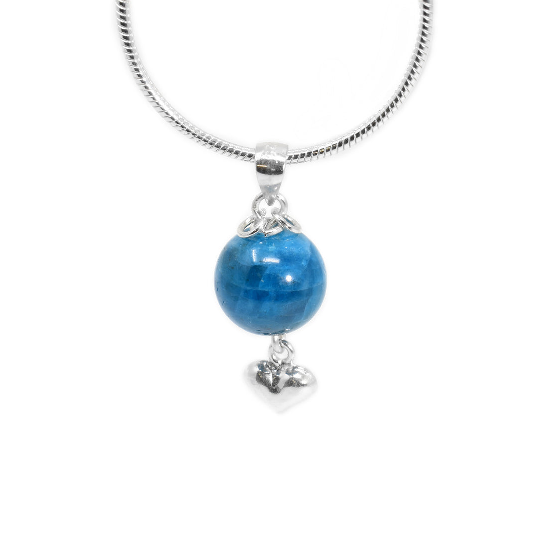 Round apatite pendant with small silver puff heart adornment hanging below. Two small, silver ring adornments hang off bail. Metal is sterling silver.