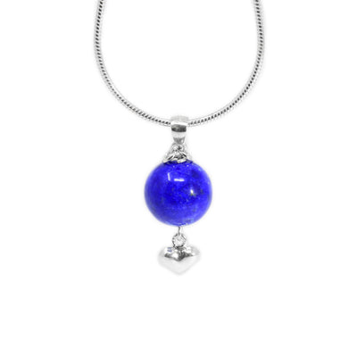Round lapis lazuli pendant with small silver puff heart adornment hanging below. Two small, silver ring adornments hang off bail. Metal is sterling silver.