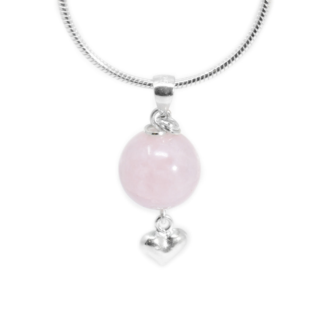 Round rose quartz pendant with small silver puff heart adornment hanging below. Two small, silver ring adornments hang off bail. Metal is sterling silver.