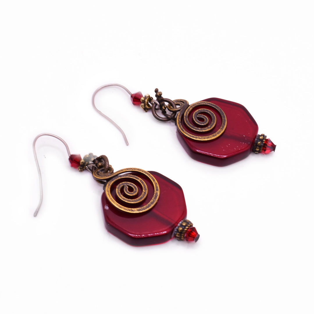 Hexagonal Red Glass with a brass spiral hanging on front. Bicone red Austrian crystals on top and bottom. Brass adornments below and above crystals.