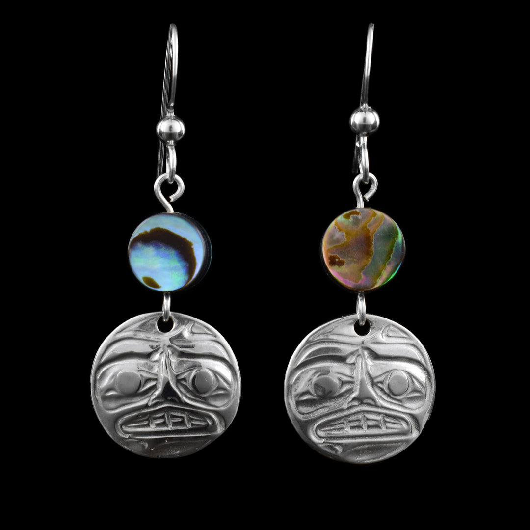 The round dangle sterling silver moon earrings have expressive facial features, raised eyes, a nose, and a slightly open mouth with visible teeth. The earring includes a polished abalone bead above the silver charm. The shell displays colours of blues, purples, greens, and browns. Dangle Earrings with fishhook ear wires for easy wearing.