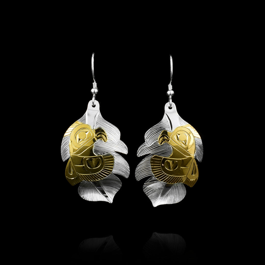 These gold Owl earrings have wide, sterling silver hangs that are shaped like owl feathers. There are carvings on their surface detailing the feathers. the owl is shown on the hangs using 14K gold plating. its eye, beak and feather details on the wing and tail are detailed.