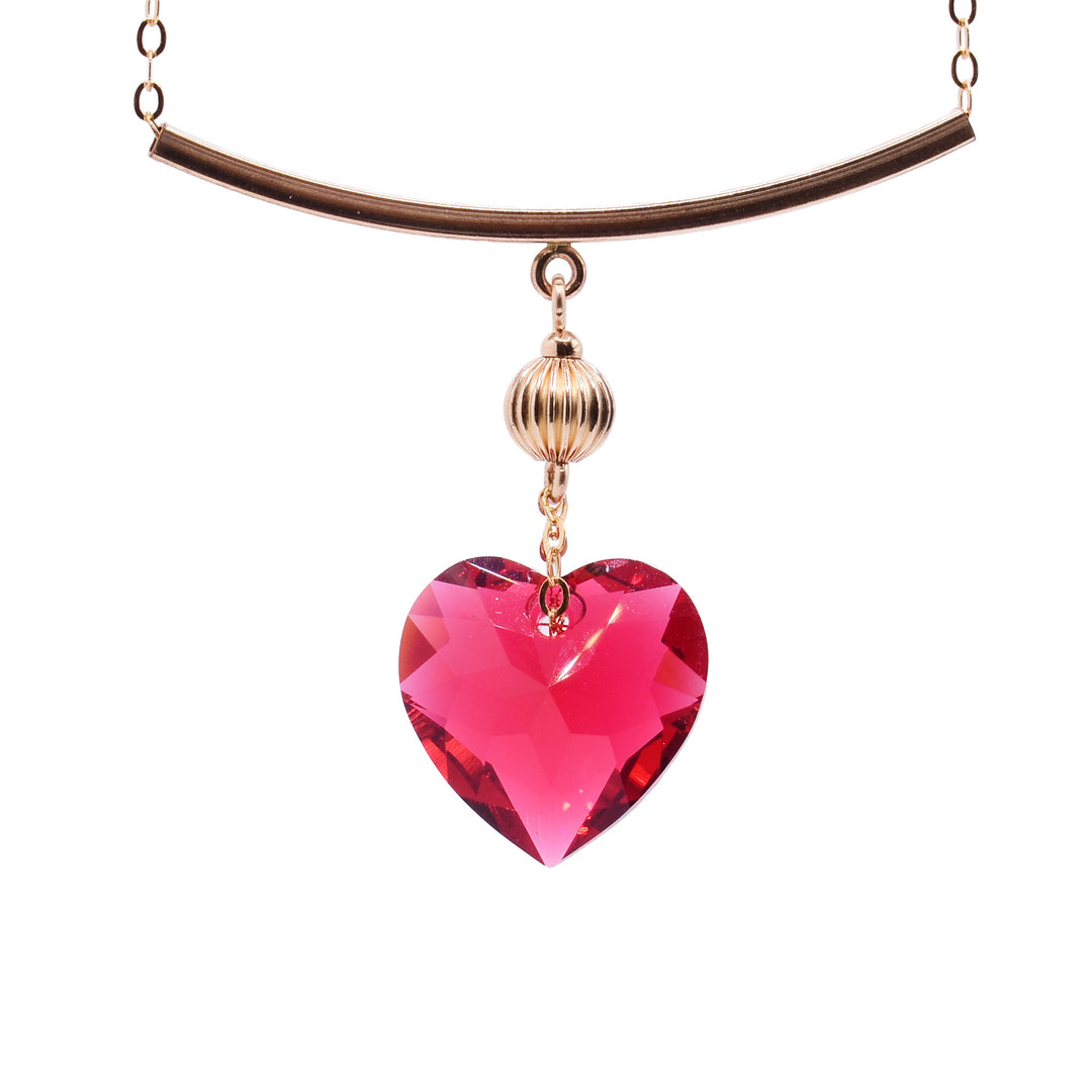 This Scarlet Swarovski crystal heart necklace has a heart shaped, crystal pendant dangling from a 14K gold filled charm that is attached to a horizontal, thin and curved pendant. The chain runs through the horizontal pendant which displayed the crystal pendant more prominently.
