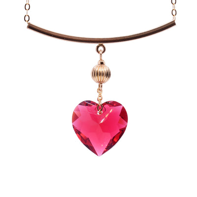 This Scarlet Swarovski crystal heart necklace has a heart shaped, crystal pendant dangling from a 14K gold filled charm that is attached to a horizontal, thin and curved pendant. The chain runs through the horizontal pendant which displayed the crystal pendant more prominently.