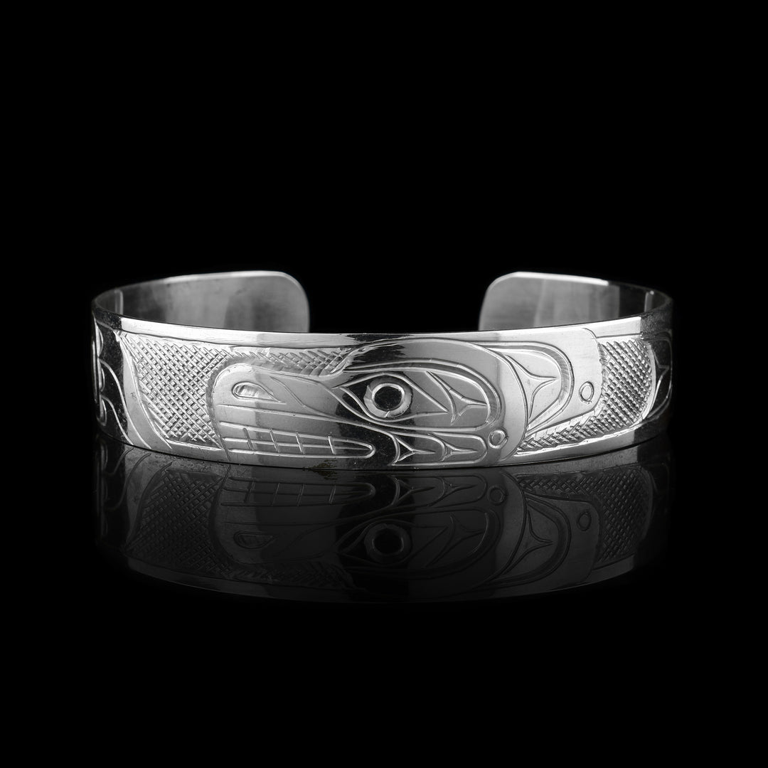 This sterling silver cuff has a single band what a gap in the back. The Bear's head is depicted in a side veiw in the center of the piece and takes up the width of the band. To either side of the head, which faces left, one of its clawed paws is depicted. The paws are facing the head and there are cross hatching patterns made in the background of the piece.