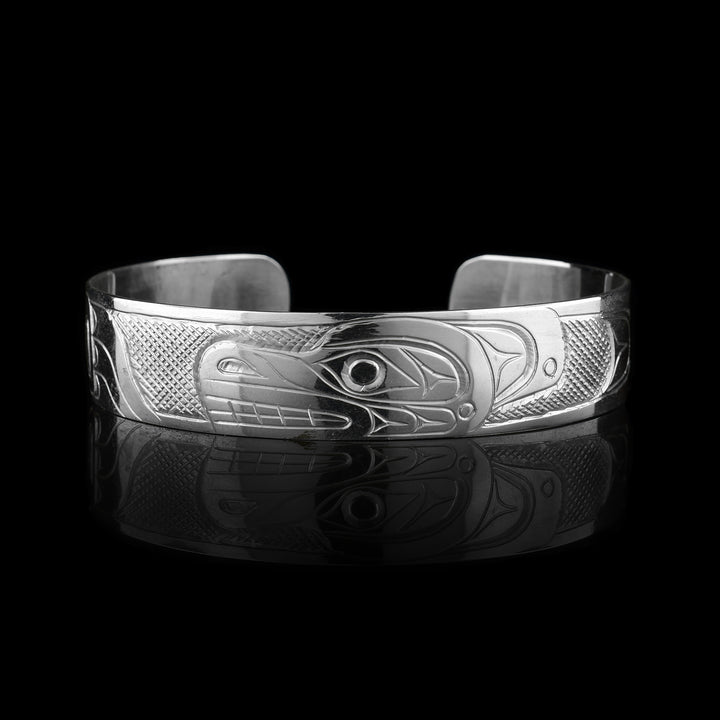 This sterling silver cuff has a single band what a gap in the back. The Bear's head is depicted in a side veiw in the center of the piece and takes up the width of the band. To either side of the head, which faces left, one of its clawed paws is depicted. The paws are facing the head and there are cross hatching patterns made in the background of the piece.