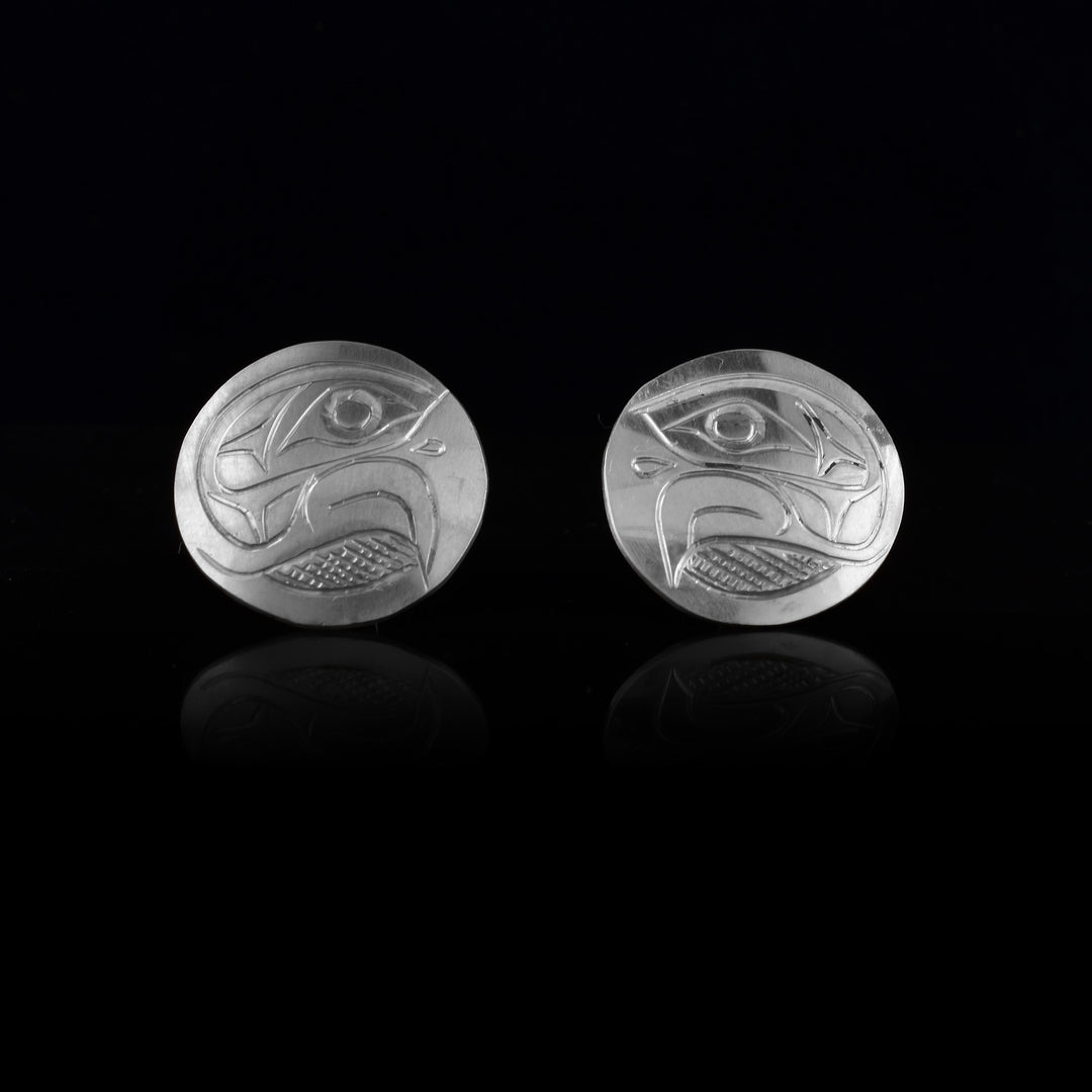 These Eagle stud earrings are made from sterling silver and are circle shaped. There are carvings of the side profile of the head of the Eagle legend made into the surface of the pieces. In the space behind the head, there are cross hatching patterns.