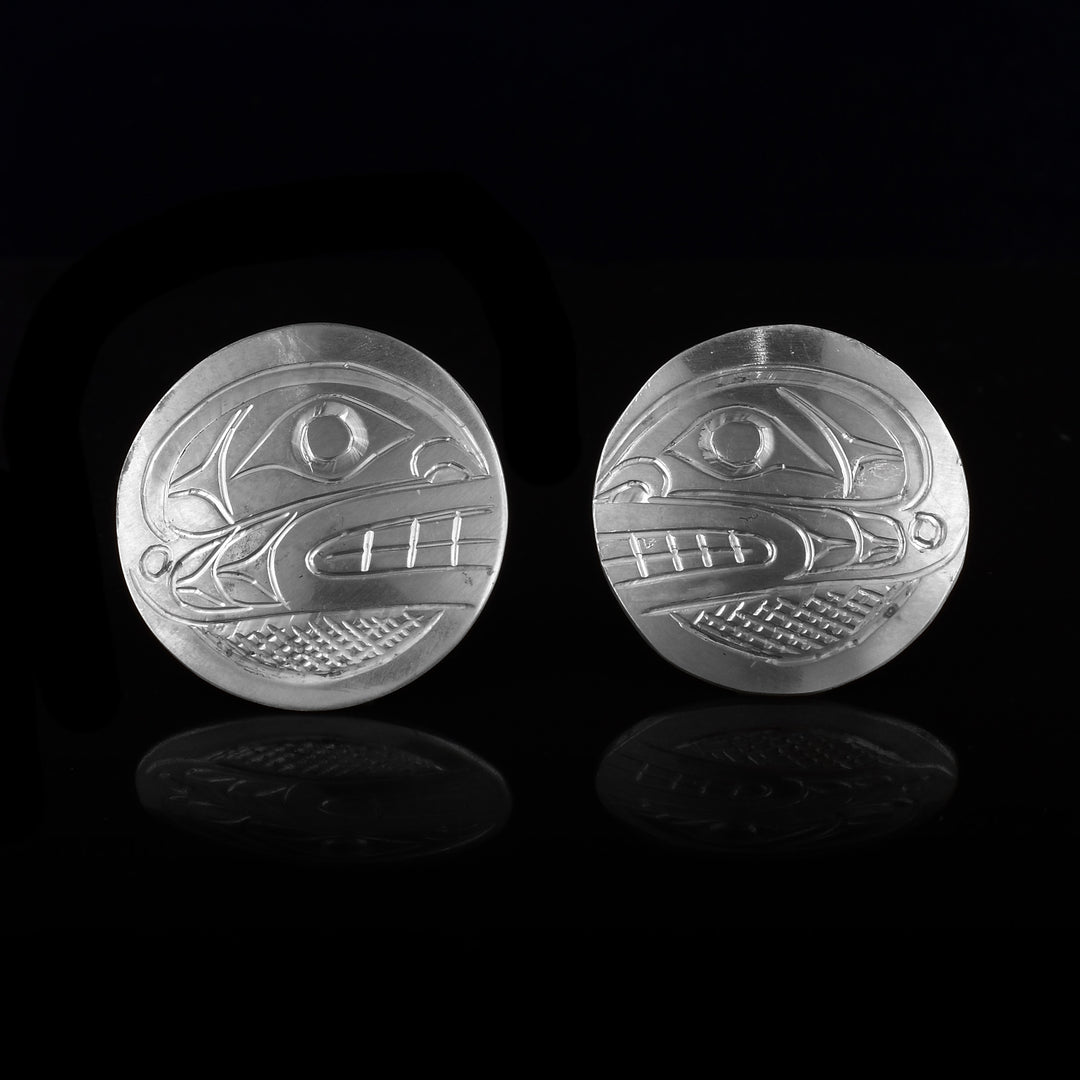 These Orca stud earrings are made from sterling silver and are circle shaped. There are carvings of the side profile of the head of the Orca legend made into the surface of the pieces. In the space behind the Orca head, there are cross hatching patterns.