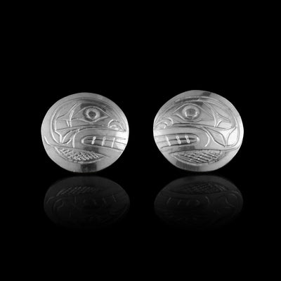 These Orca stud earrings are made from sterling silver and are circle shaped. There are carvings of the side profile of the head of the Orca legend made into the surface of the pieces. In the space behind the head, there are cross hatching designs.