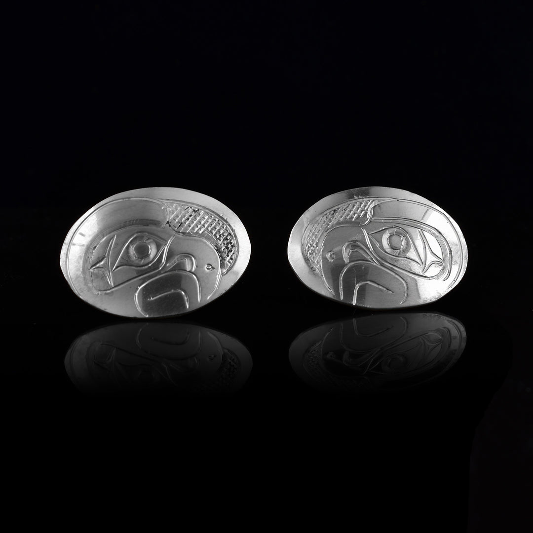 These Eagle stud earrings are made from sterling silver and have la, horizontal and oval shaped surfaces. There are depictions of the side profile of the head of the Eagle legend carved into the earrings. In the space behind the Eagle head, there are cross hatching designs.