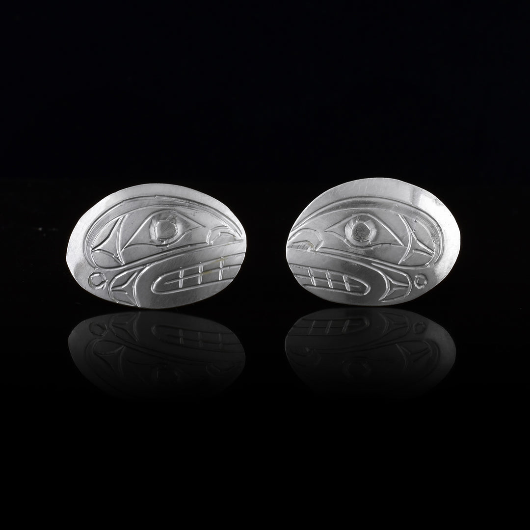 These Orca stud earrings are made from sterling silver and have wide, horizontal and oval shaped surfaces. There are depictions of the side profile of the head of the Orca legend carved into the earrings. You can see the legends bold eyes and teeth.