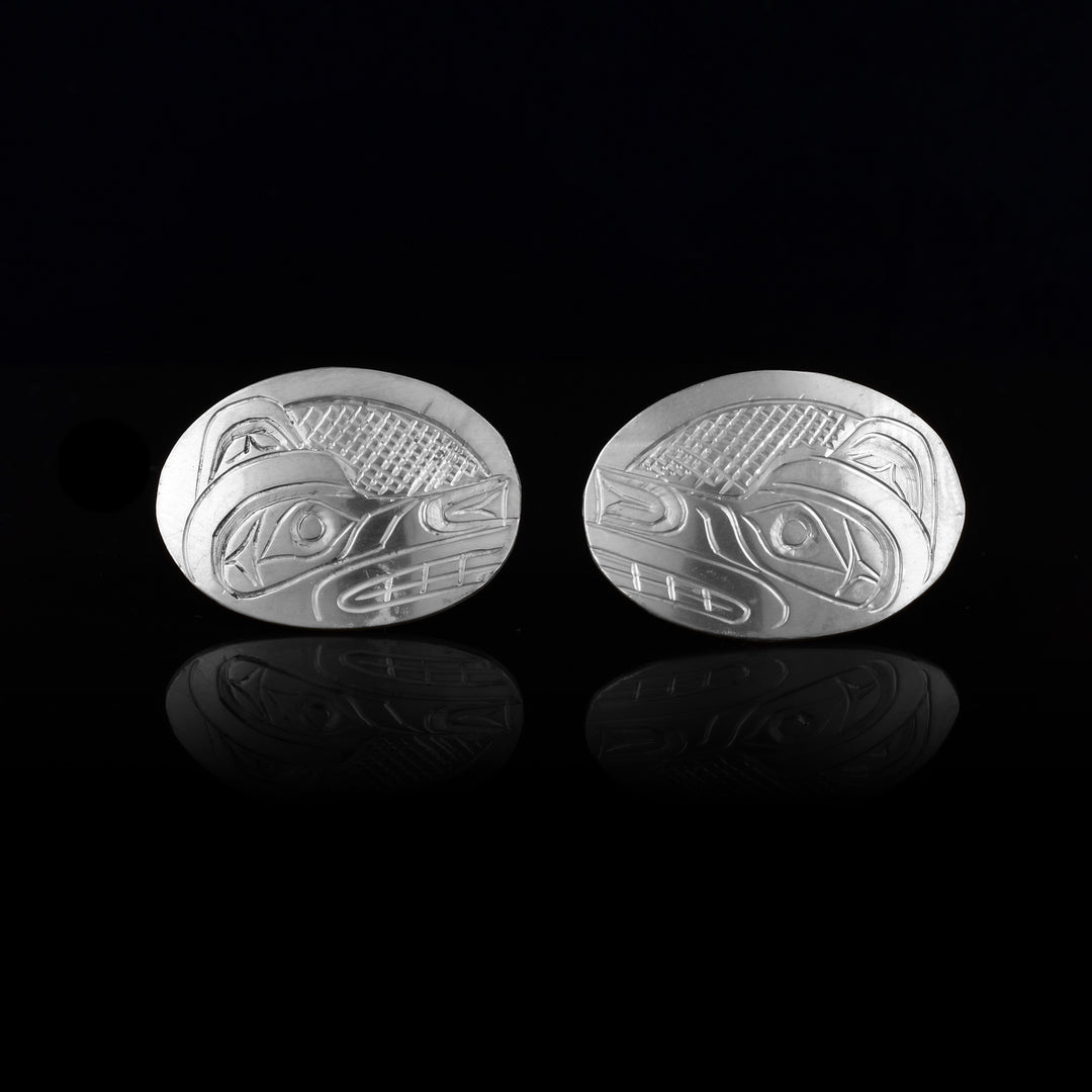 These Wolf stud earrings are made from sterling silver and have wide, horizontal and oval shaped surfaces. There are depictions of the side profile of the head of the Wolf legend carved into the earrings. In the space behind the Wolf head there are cross hatching designs.