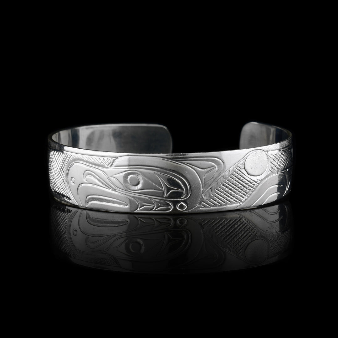 This sterling silver cuff Thunderbird bracelet has a single band what a gap in the back. The head of the Thunderbird is carved in the center of the band and has fierce beak and eye details. There are cross hatching patterns detailing its wings which extend on both sides of the band.