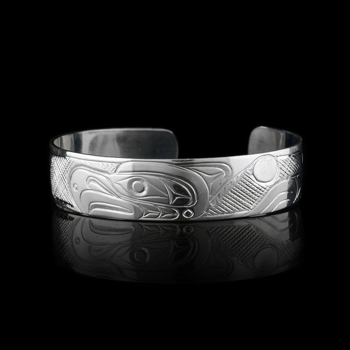 This sterling silver cuff Thunderbird bracelet has a single band what a gap in the back. The head of the Thunderbird is carved in the center of the band and has fierce beak and eye details. There are cross hatching patterns detailing its wings which extend on both sides of the band.