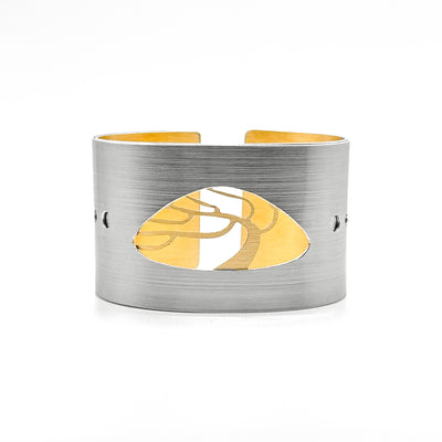 Grey cuff with cut-out smooth, triangular shape. Swaying, gold-colour tree with naked branches in cut-out from second layer. Cut out circles on sides along middle with gold-colour layer showing.