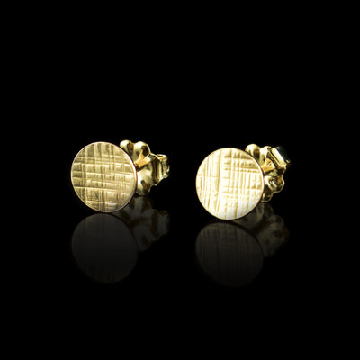 These gold circle stud earrings are made from 14K gold filled material and have flat, circle shaped studs. There are cross hatching patterns carved on the surface of the studs. The circle are bent slightly.