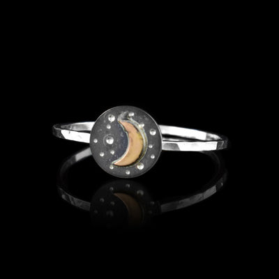 This crescent moon ring has a thin, sterling silver band with a silver circle on top of it. There are dimples made on the circle representing stars and there is a crescent moon made from 14K gold filled material in the center of the piece.