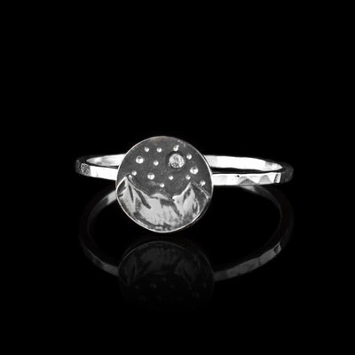 This mountain ring s made from sterling silver and has a very thin band. There is a larger, circle shaped piece on the band and there is a three peak mountain range on it. Above the mountains, there are dots made into the surface that resemble stars and the moon.