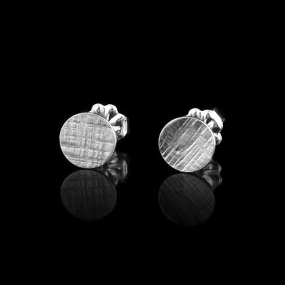 These silver circle earrings are made from sterling silver and have flat, circle shaped studs. There are cross hatching patterns carved on the surface of the studs. The circles are bent slightly.