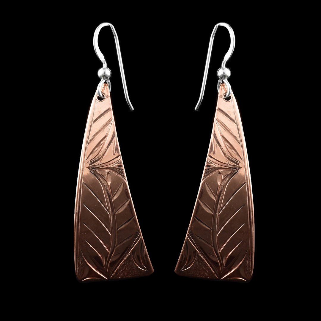 These flower copper dangle earrings feature a graceful hand-carved floral pattern that have  natural curves and flow of petals. Shaped in a tapered, trapezoidal form, the design showcases symmetrical leaf-like engravings that rise from the base and meet at a central floral point, creating a balanced look. Finished with sterling silver ear wires.
