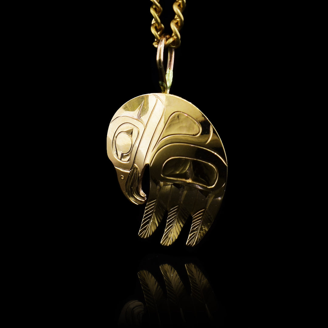 This round 14K gold Eagle pendant has the head of the Eagle at the top and a broad wing coming down from the bottom of the piece. There are three feathers coming off of the wing. There are intricate carvings on the surface of the piece depicting the Eagle.
