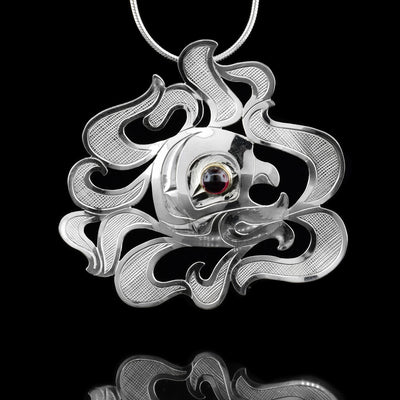 This sterling silver pendant is shaped like and has carvings on the surface of it that depict the Wind Spirit. The Wind Spirit is depicted being in the middle of many decorative "wind gusts". The eye of the Wind Spirit is a large garnet gemstone mounted on 14K gold.