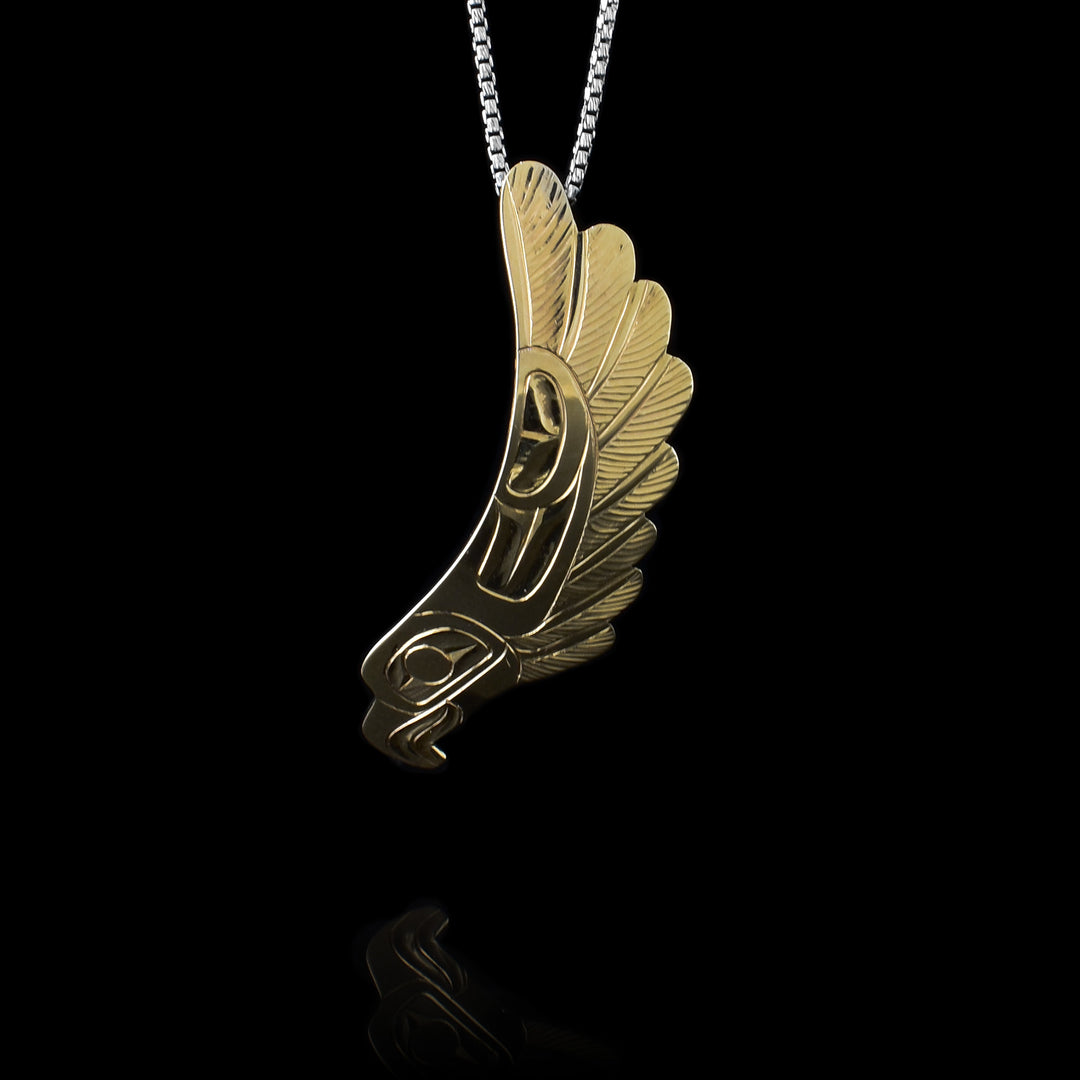 This 14K gold pendant is long and drops down. At the bottom, the head of the Eagle is depicted and it curves up with feathers running up the side of the piece. There are carvings on the surface detailing the feather and the face of the pendant.