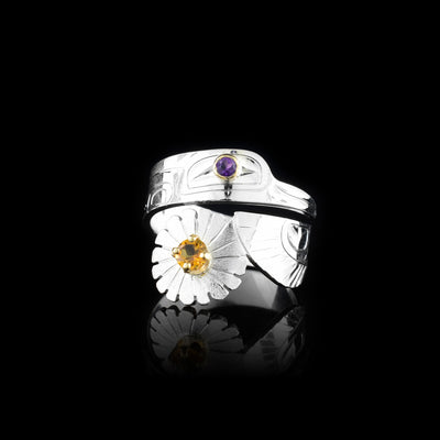 This Hummingbird ring is made from sterling silver and has a single band that wraps around the finger twice. There are carvings on the sirafec of the piece depicting the Hummingbird. The head is on the top and the wing with a daisy is at the bottom. There is an amethyst gem in the eye and a citrine gem in the center of the flower.