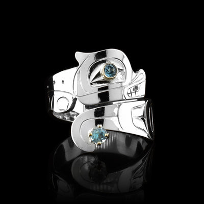 This Otter sterling silver blue topaz ring has a wide band that wraps around the finger twice. The top band is carved to depict the head of the Otter and the bottom one depicts its tail. There are blue topaz gems that are embedded into the eye of the legend and in the center of its tail. There are 14K gold highlights around the eye of the Otter.
