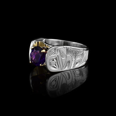 Solitaire Eagle Ring with amethyst by Fred Myra. The artist has hand-carved the profile of two Eagle bodies on either side of the amethyst he has set in the center of the ring. The background of the ring has been hand-carved into a neat crisscross pattern to allow for the Eagles to stand out. The round amethyst has been set using a 14k gold claw setting. The ring tapers down at the back.