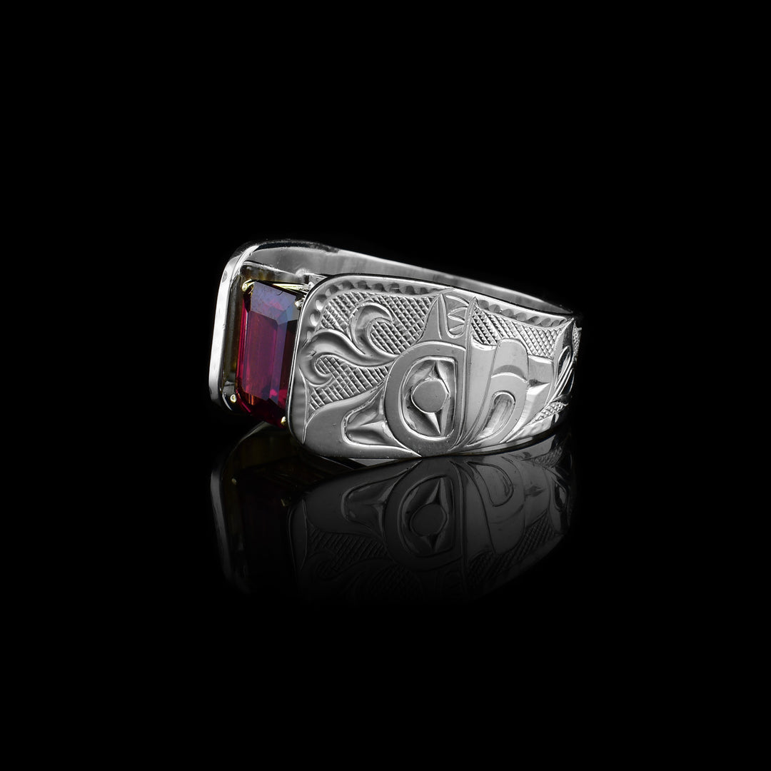 This Orca ring has a wide and tapered band that extends in cathedral style above the rhodolite garnet gem that is set in 14K gold claws. There are carvings made on the band that depict the Orca. The Orca is facing the top of the ring with a water spout coming out of its head. There are cross hatching patterns in the background on the band.