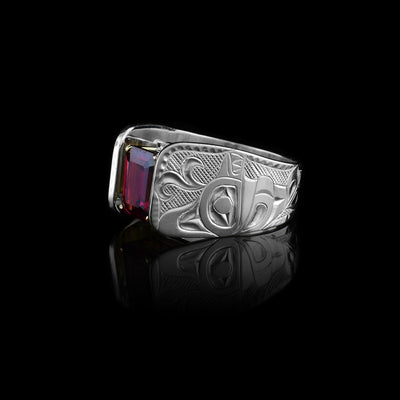 This Orca ring has a wide and tapered band that extends in cathedral style above the rhodolite garnet gem that is set in 14K gold claws. There are carvings made on the band that depict the Orca. The Orca is facing the top of the ring with a water spout coming out of its head. There are cross hatching patterns in the background on the band.