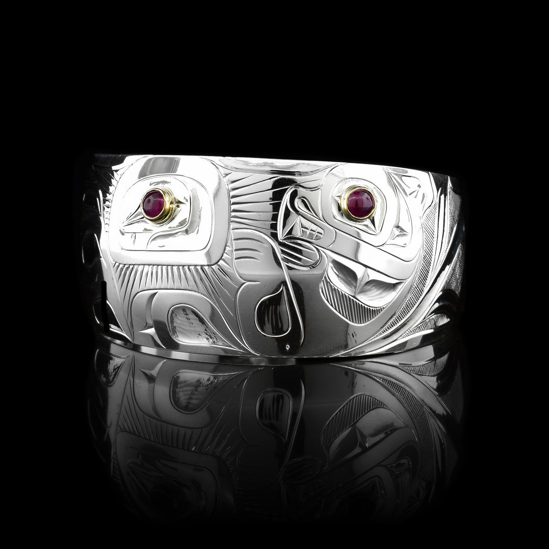This unique urchin and Otter bracelet has a single, wide and tapered band with a gap in the back. There is a depiction of the Otter holding a sea urchin that has been carved into the surface of the band. There are rubies held in 14K gold in the eye of the Otter and in the urchin.