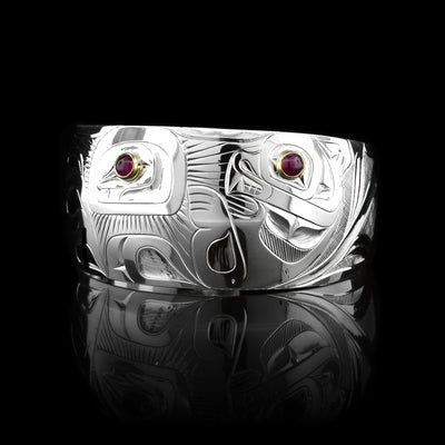 This unique urchin and Otter bracelet has a single, wide and tapered band with a gap in the back. There is a depiction of the Otter holding a sea urchin that has been carved into the surface of the band. There are rubies held in 14K gold in the eye of the Otter and in the urchin.