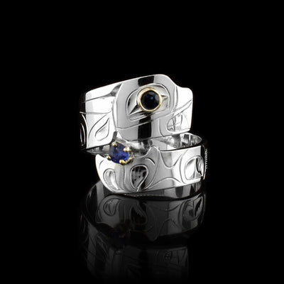 This Orca ring has a sterling silver and thin band that wraps around the finger twice. A depiction of the head of the Orca has been carved into the top band of the piece and its tail is depicted at on the bottom band. There is a black tourmaline gem embedded in 14K gold for the eye of the legend.