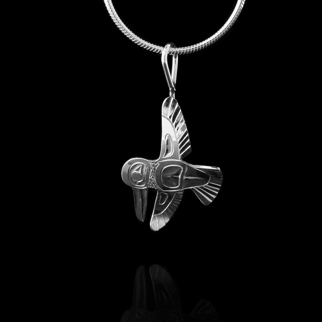 This flying Hummingbird pendant is made using sterling silver and is shaped like a Hummingbird in flight. The wings are straight up and straight down and the head is facing down. There are carvings on the pieces depicting the Legend.