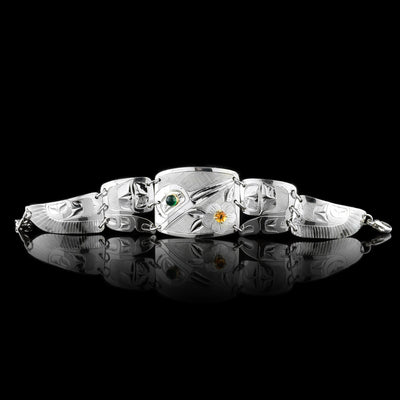 This beautiful panel bracelet has a sterling silver, rectangle panel with a depiction of the Hummingbird and a flower carved into it. There is a green onyx gem in the eye of the legend and a citrine gem in the center of the flower. There are two other panels on either side of the center one that taper. There are designs carved into these panels with the last ones depicting wings of the Hummingbird.