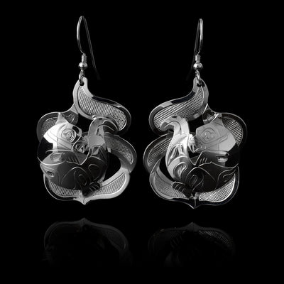 The Otter earrings are made using sterling silver and have abstract hangs depicting the Otter legend in ocean waves. The otter is curled up on its back with its tail above its head. The waves are made with cutout pieces and the Otter is set in the front of then. There are carvings made on the piece depicting the scene.
