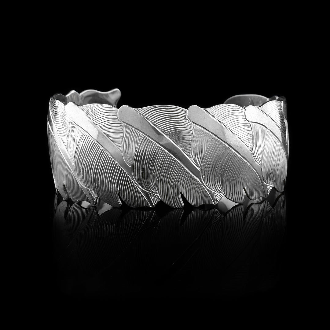 This sterling silver cuff bracelet is shaped like and has carvings on its surface that depict multiple owl feathers wrapping around the band.