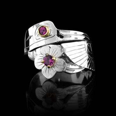 This Hummingbird ring has a sterling silver wide band that wraps around the finger twice. The top band is carved to depict the head of the Hummingbird and the bottom one depicts its wing with a flower beside it.. There is are rhondite garnet gems that are embedded in 14K gold in the eye of the legend and the flower at the bottom of the piece.