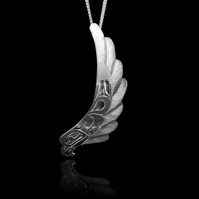 The swooping Eagle pendant is made with sterling silver and depicts the Eagle in flight. The piece is long and the head of the Eagle is depicted at the bottom and its wing is curved and outstretched across the rest of the piece. There are carvings on the surface of the piece depicting the Eagle.