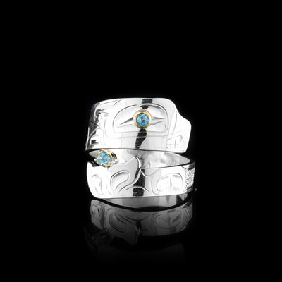 This blue topaz ring has a sterling silver band that wraps around the finger twice. The piece depicts the Orca and there are details of the legend carved into the band. The head is at the top with a blue topaz gem set in the eye and the bottom is the tail with another gem held in it.