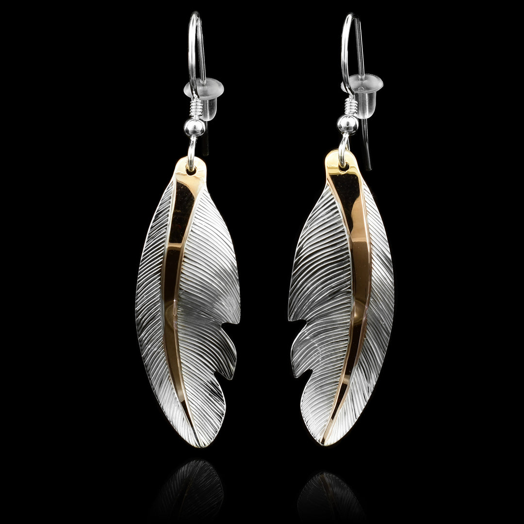 These dangling feather earrings have hangs that are feather shaped and have intricate carved details on the surface of it. There is 18K gold plating on the center part of the feather.