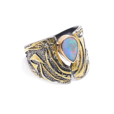 This sterling silver opal ring has designs carved into it. There are 24K gold highlights on the band and a teardrop shaped opal gem wrapped in 14K gold.