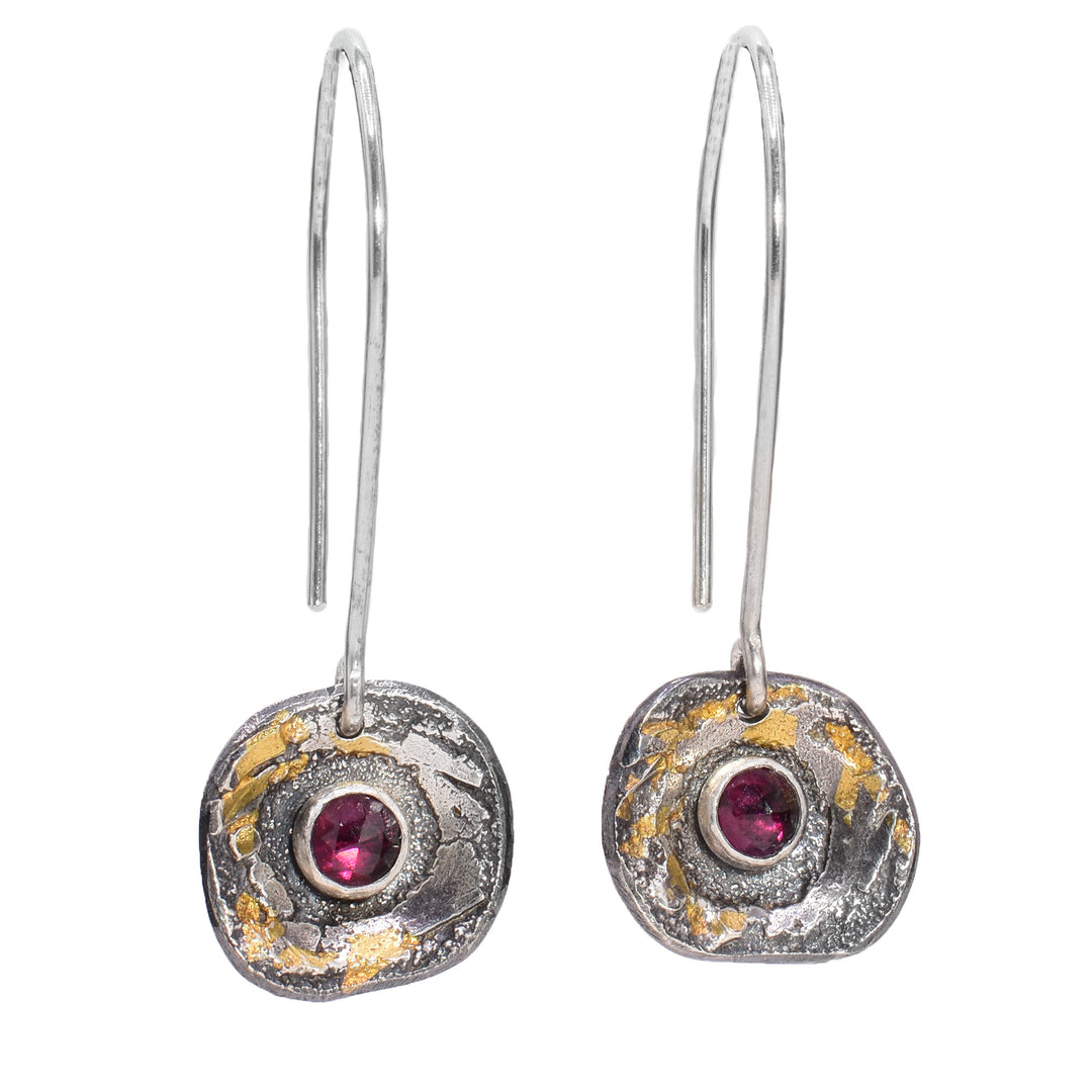 These sterling silver garnet earrings have small circles attached to the hooks. These hangs have a textured surface with 24K gold highlights and a garnet gemstone in the middle.