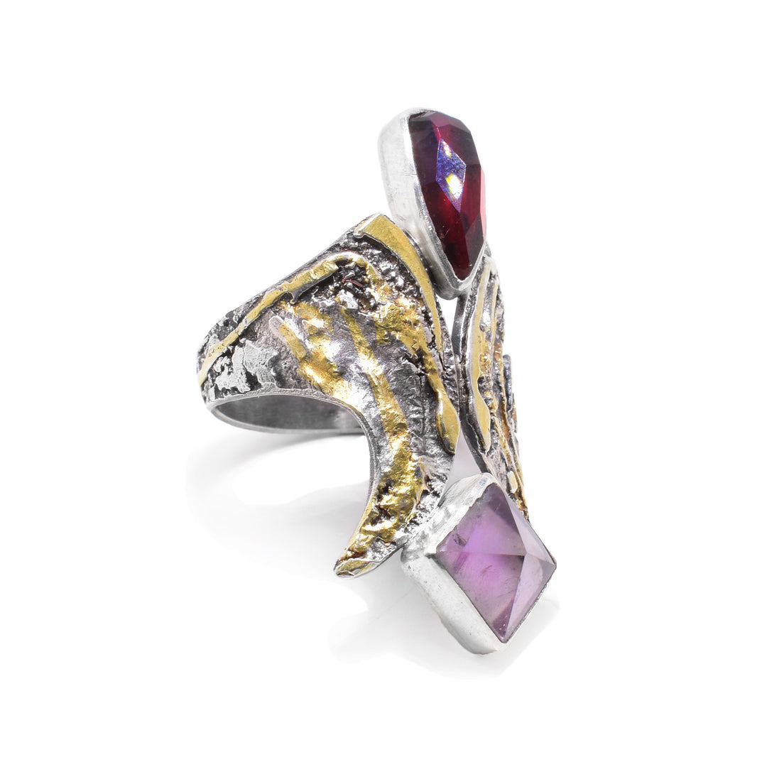 This amethyst ring is made from sterling silver and has 24K gold highlights. Held between band are large garnet and amethyst gemstones. 