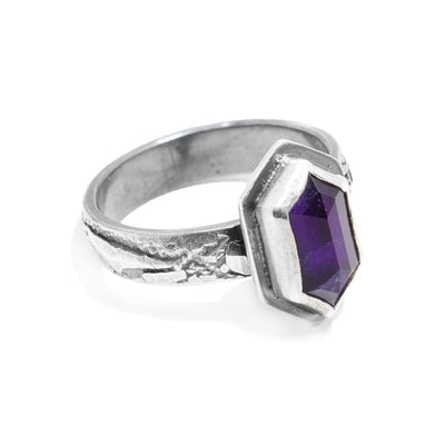 This sterling silver amethyst ring has a textured band with a hexagon amethyst gem embedded in a silver hexagon.