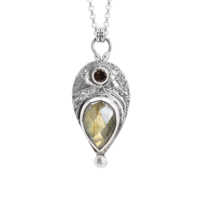 This smoky quartz necklace has a sterling silver teardrop pendant with designs carved into it. There is a garnet gem and a teardrop shaped smoky quartz gem.