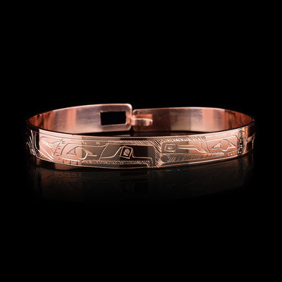 This copper bangle bracelet has a single, thin band with a simple hook clasp in the back. There is a depiction of the Raven and the Eagle that have been beautifully carved into the surface of the band. The heads of the legends meet and are facing each other at the top of the band.