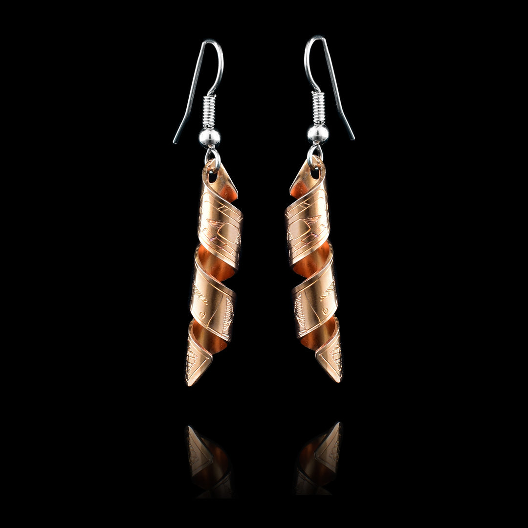 These spiral earrings have hangs made from copper bands that have been curved into horizontal spirals. The copper cylinders drop down and there is a depiction of the Orca carved into the outside of the bands. The head of the Orcas are facing the top of the piece.